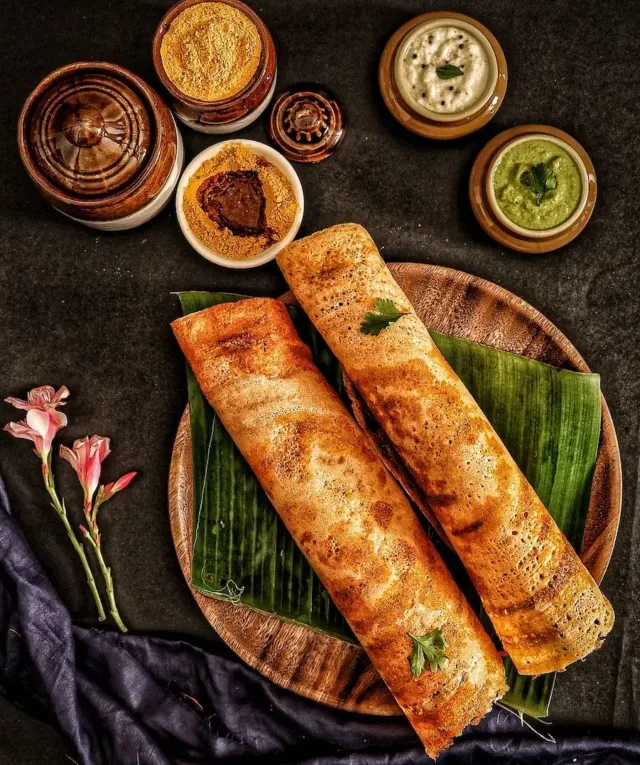 A Pair of dosas on a Wooden Tray with Banana Leaf