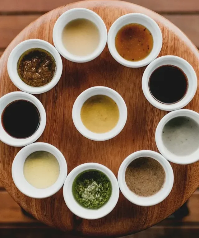 a wooden table topped with white cups filled with sauces
